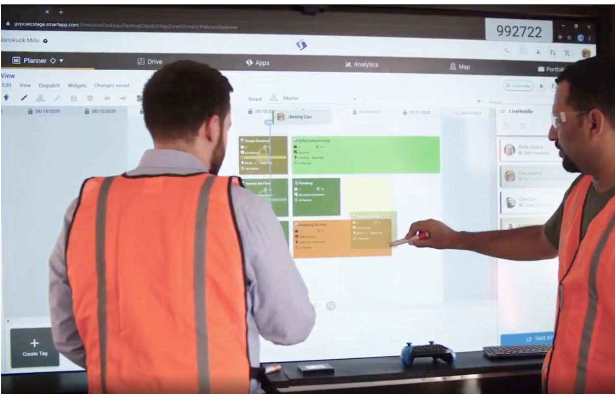 Two workers collaborating at a SmartApp planner board on a large touchscreen